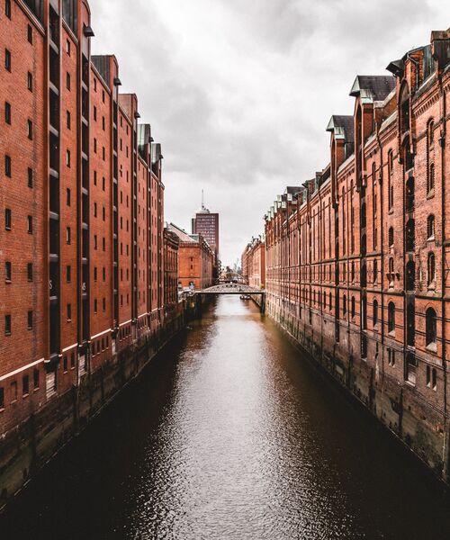 Wasserweg zwischen den roten Backsteingebäuden der Hamburger Speicherstadt unter bewölktem Himmel.